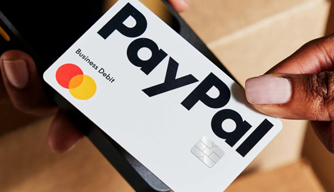 Eine Person hält eine PayPal Business Debit Mastercard auf ein Kartenlesegerät oder Smartphone.